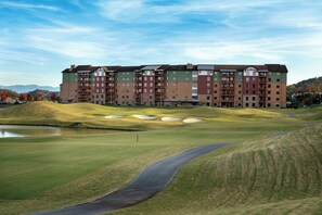 A multi-story hotel with a golf course in front, including bunkers and a pond.