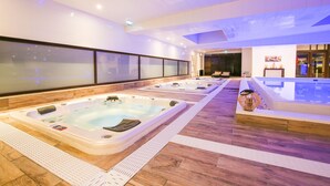 A modern indoor spa area with multiple hot tubs, wooden flooring, and a glass wall providing a view of the outside.