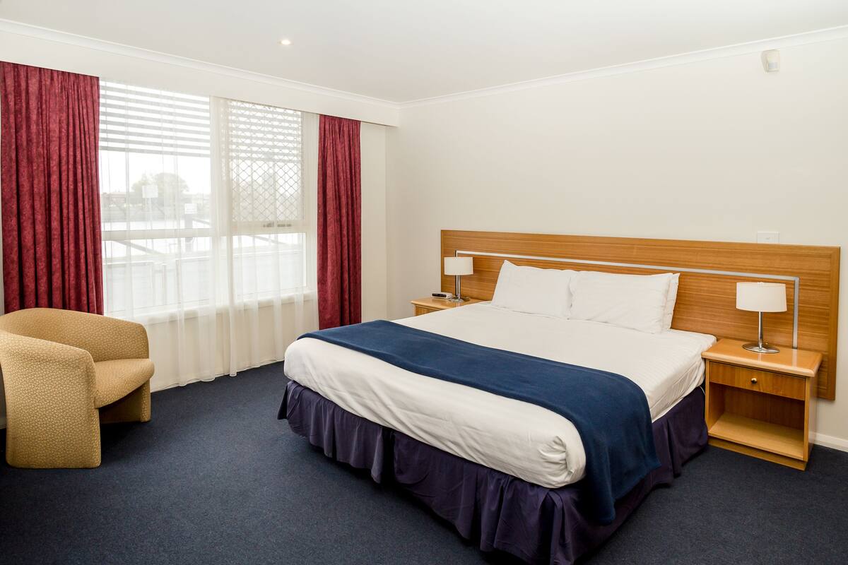 A hotel room with a large bed, two bedside tables, a chair, and a window with curtains.