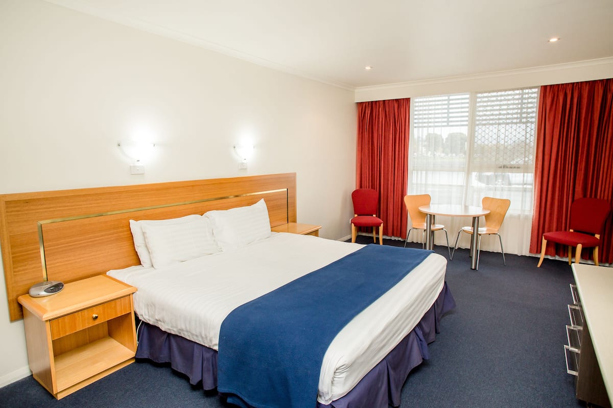 A hotel room with a large bed, a bedside table, a desk, two chairs, and a window with curtains.
