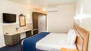 Una habitación de hotel con cama, escritorio, televisor, armario y espejo.
