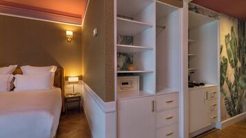 A hotel room with a bed, a nightstand, a digital clock, a wardrobe with multiple drawers, and a wall with a tropical mural.