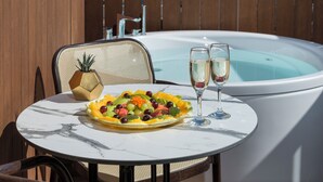 A round table with a fruit platter and two glasses of champagne, a hot tub, and a chair with a woven backrest. - Adam Boutique Eilat (Eilat)