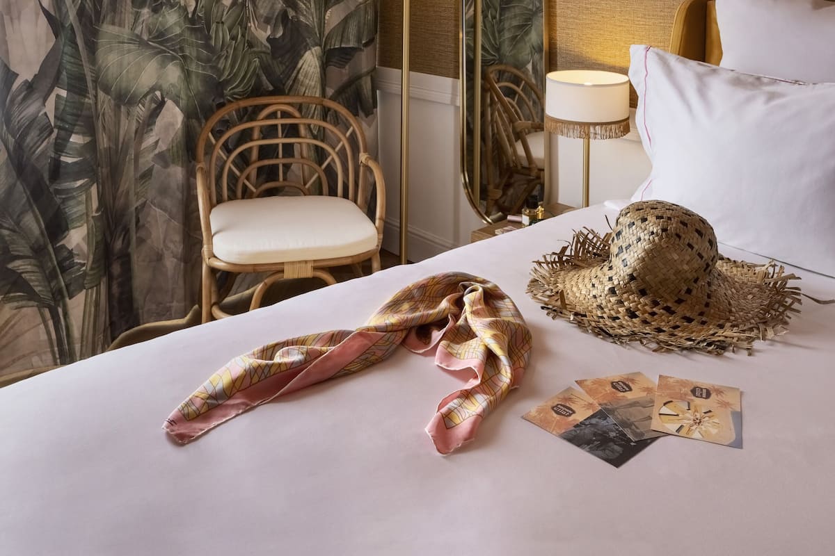 A hotel room with a bed, a chair, a lamp, and a tropical-themed curtain.