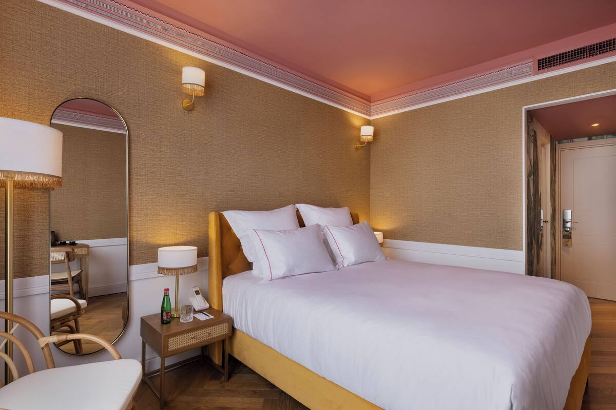 A hotel room with a large bed, a bedside table with a lamp, a chair, and a mirror.