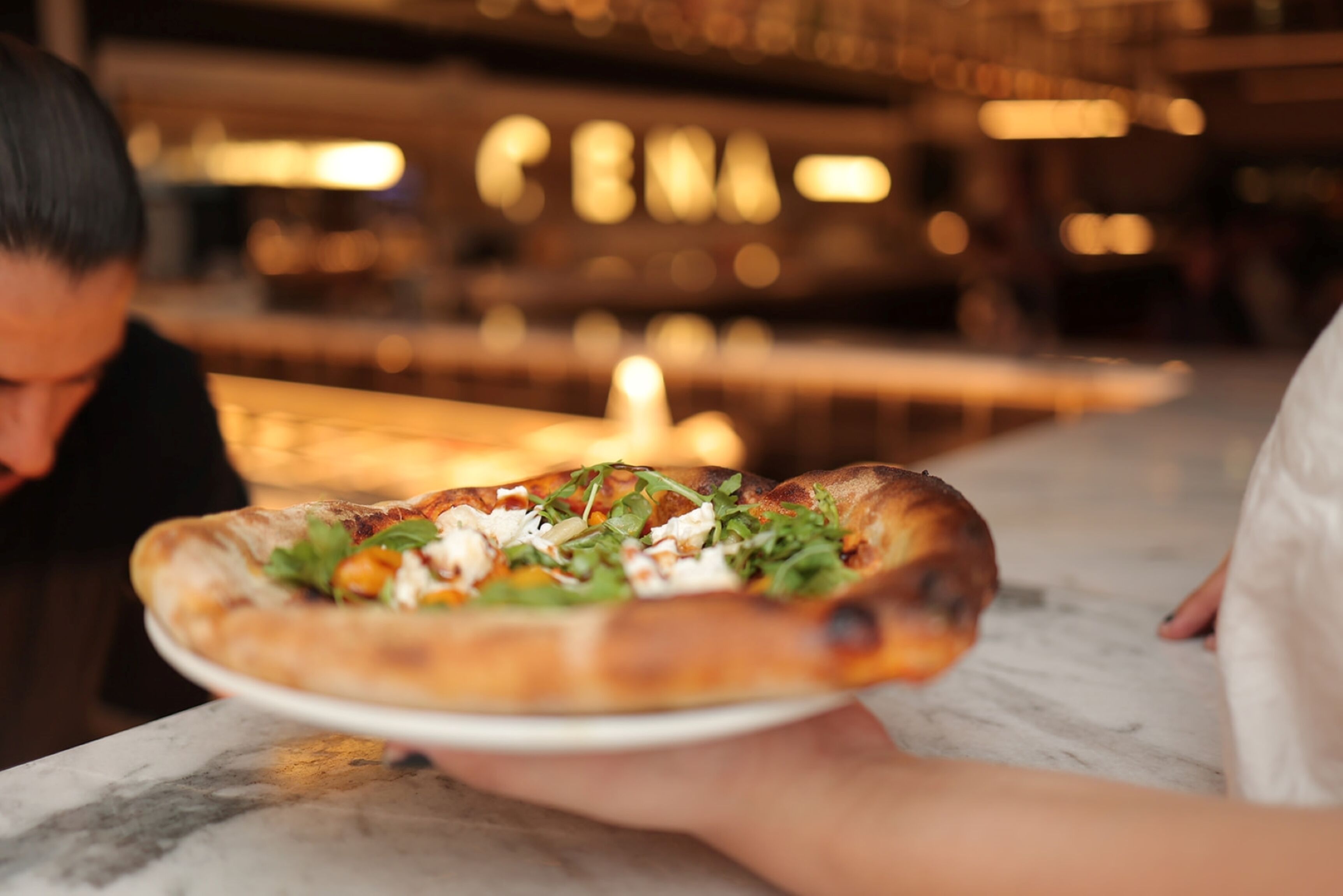 A person holding a pizza on a white plate.