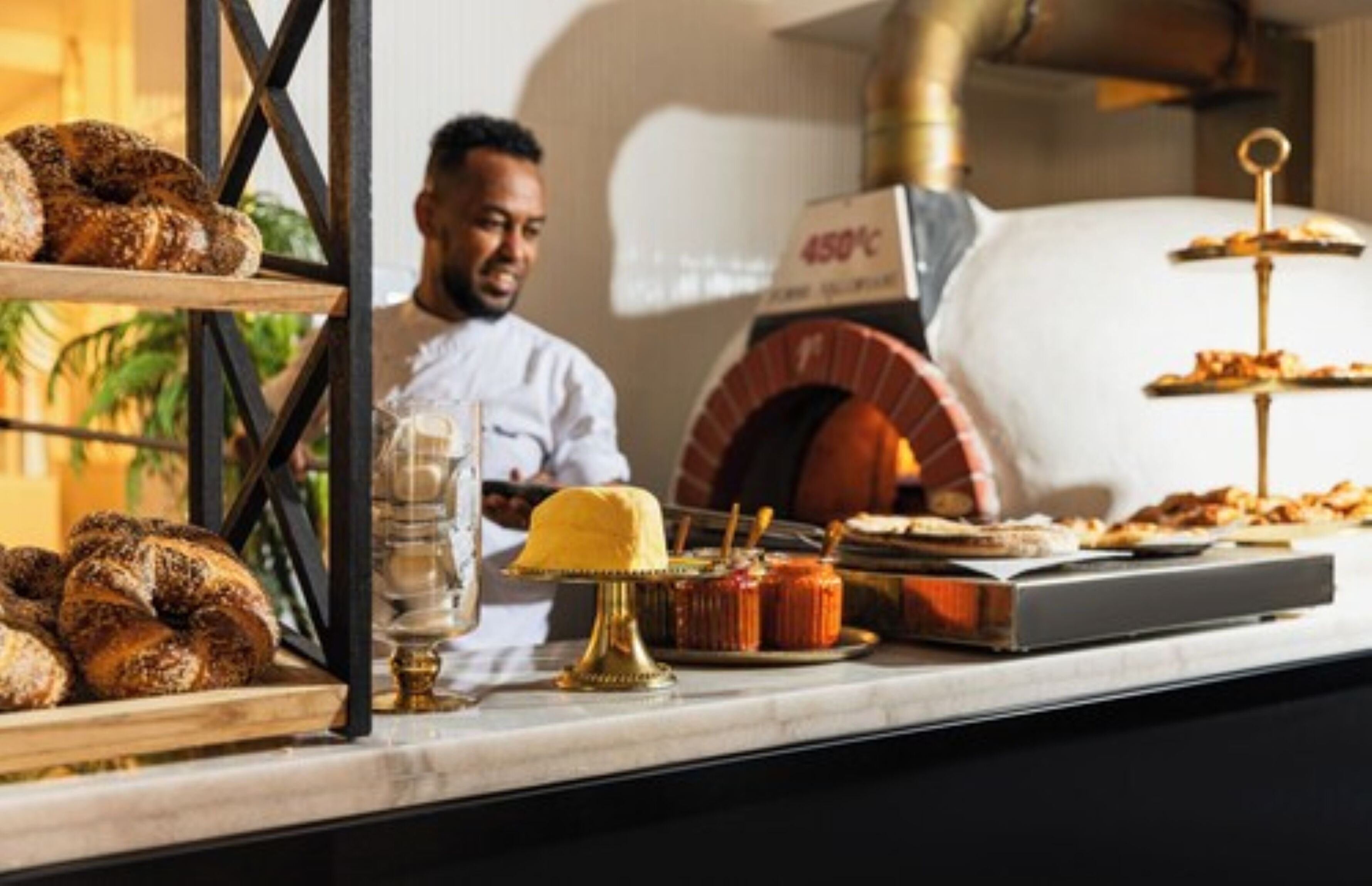 A bakery counter with pastries, a pizza oven, and a chef.