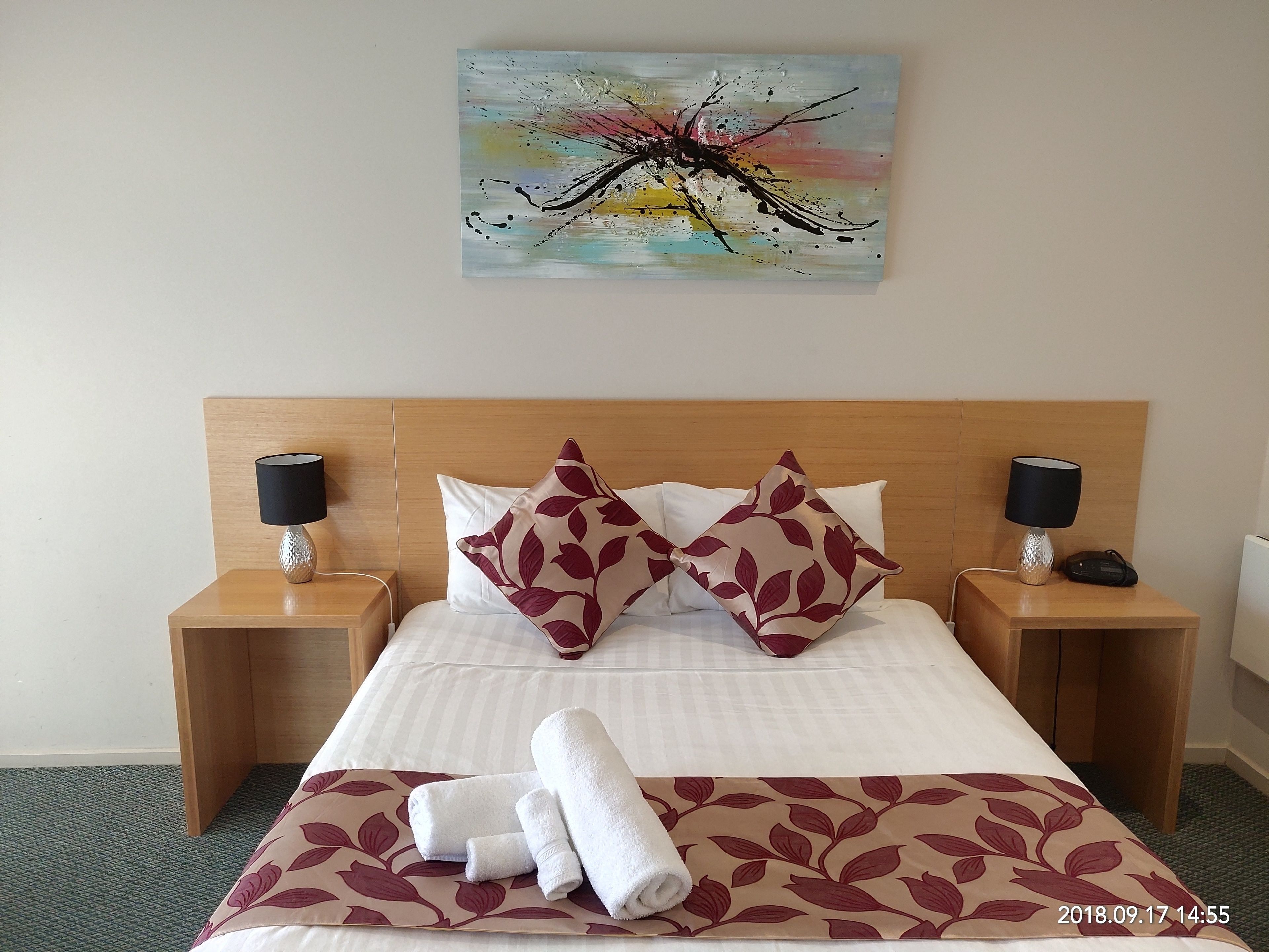 A hotel room with a bed, two nightstands, a painting, and a floral-patterned bedspread.