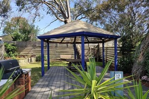 Un área de estar al aire libre techada con una mesa y sillas de madera, una parrilla y un cartel con el número 12 al frente.