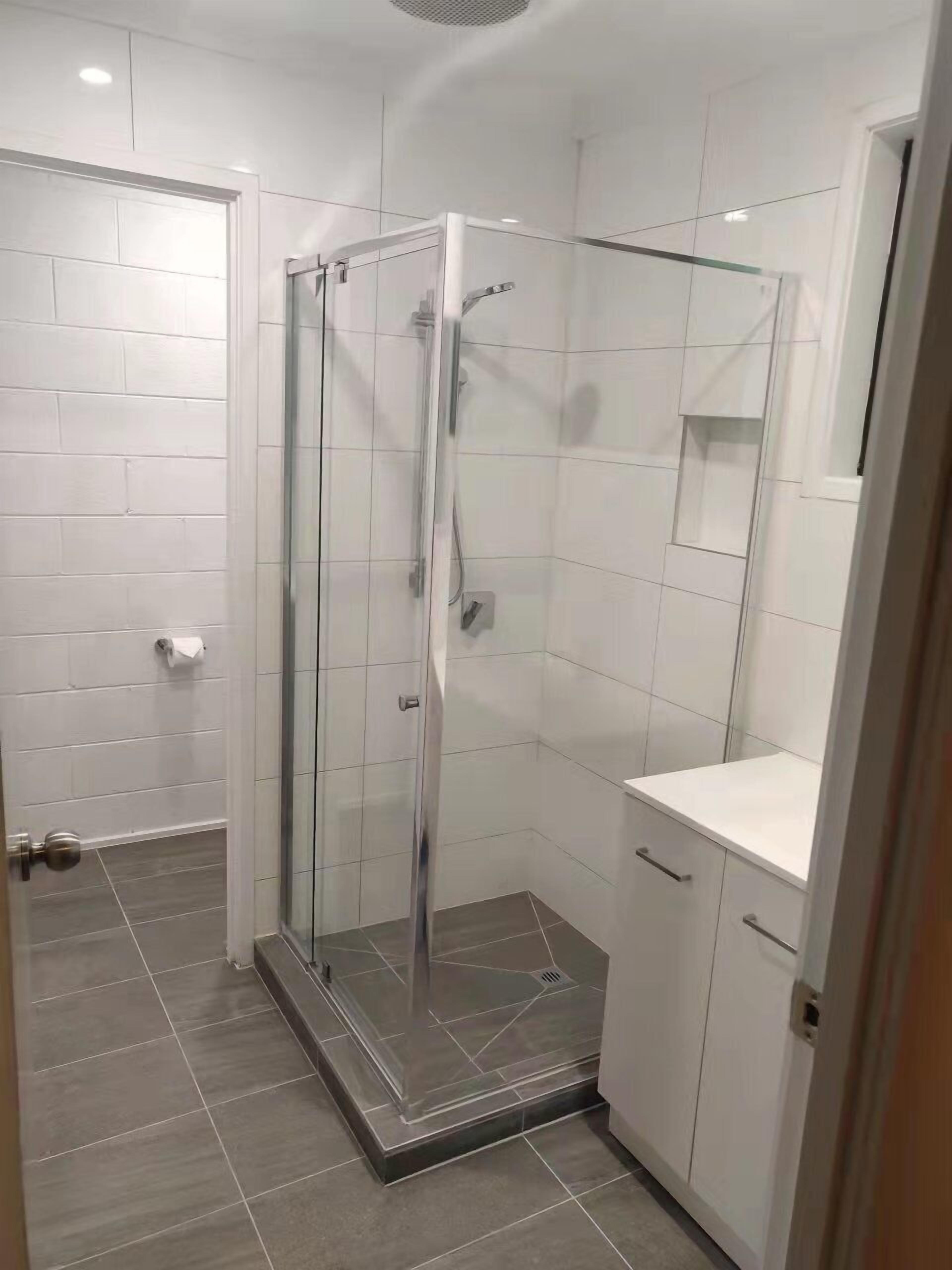 Een moderne badkamer met een douchecabine van glas, witte betegelde wanden en een grijze tegelvloer.
