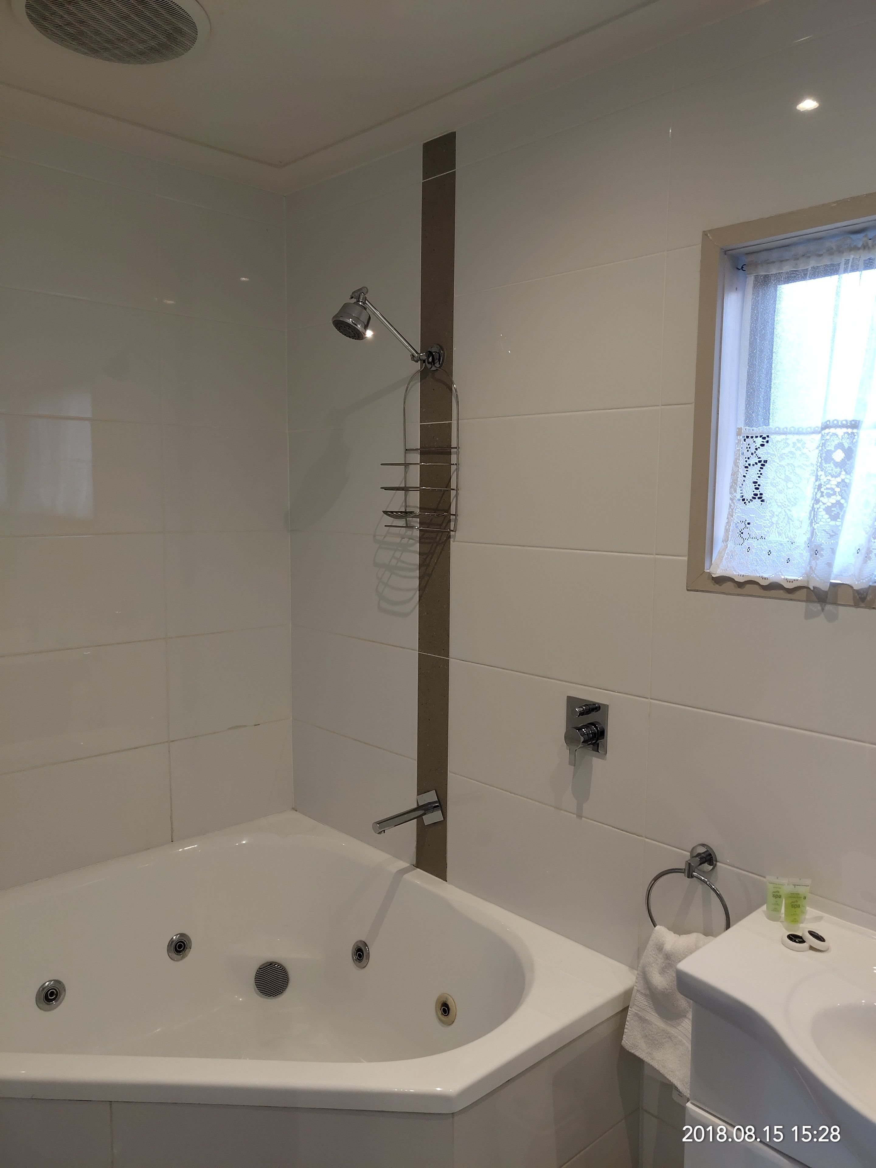 A modern bathroom with a large bathtub, a shower area, and a window with lace curtains.