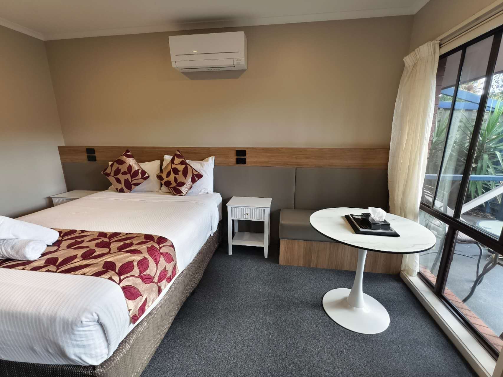 A hotel room with a bed, bedside table, and a small round table with a book and a tissue box.