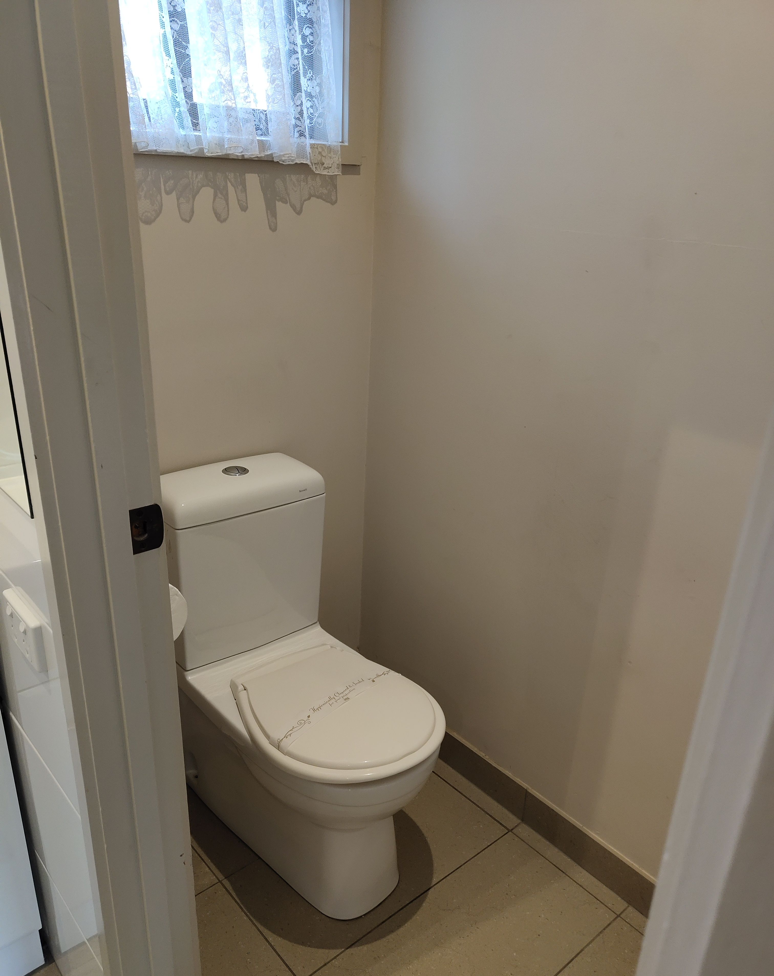 Et hvidt toilet i et badeværelse med et vindue over.