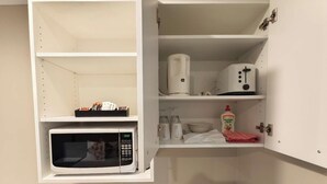 Una cocina compacta con microondas, tostadora y estante con lo esencial para cocinar.