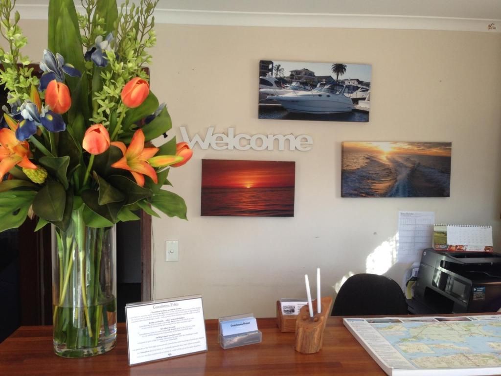 Vastaanottotiski, jossa on tervetulotoivotus, maljakko täynnä kukkia, kartta ja seinällä kehystettyjä kuvia.