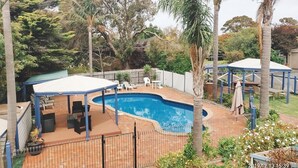 Patio trasero con piscina, zona de estar techada y palmeras.