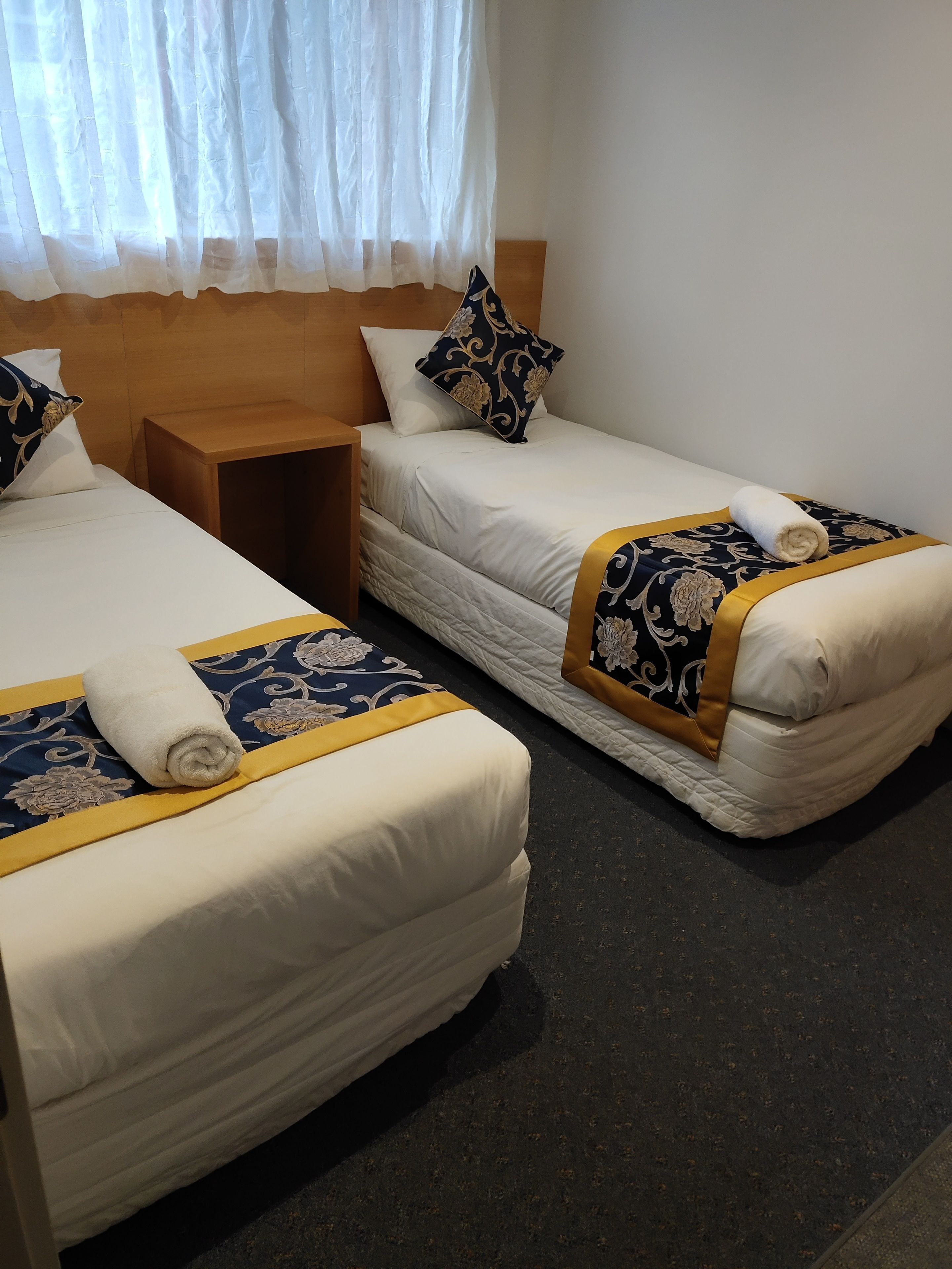 A hotel room with two beds, each with a duvet and a pillow. There is a wooden nightstand between the beds.