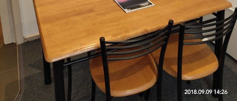 A dining area with a wooden table, four chairs, and a painting on the wall.