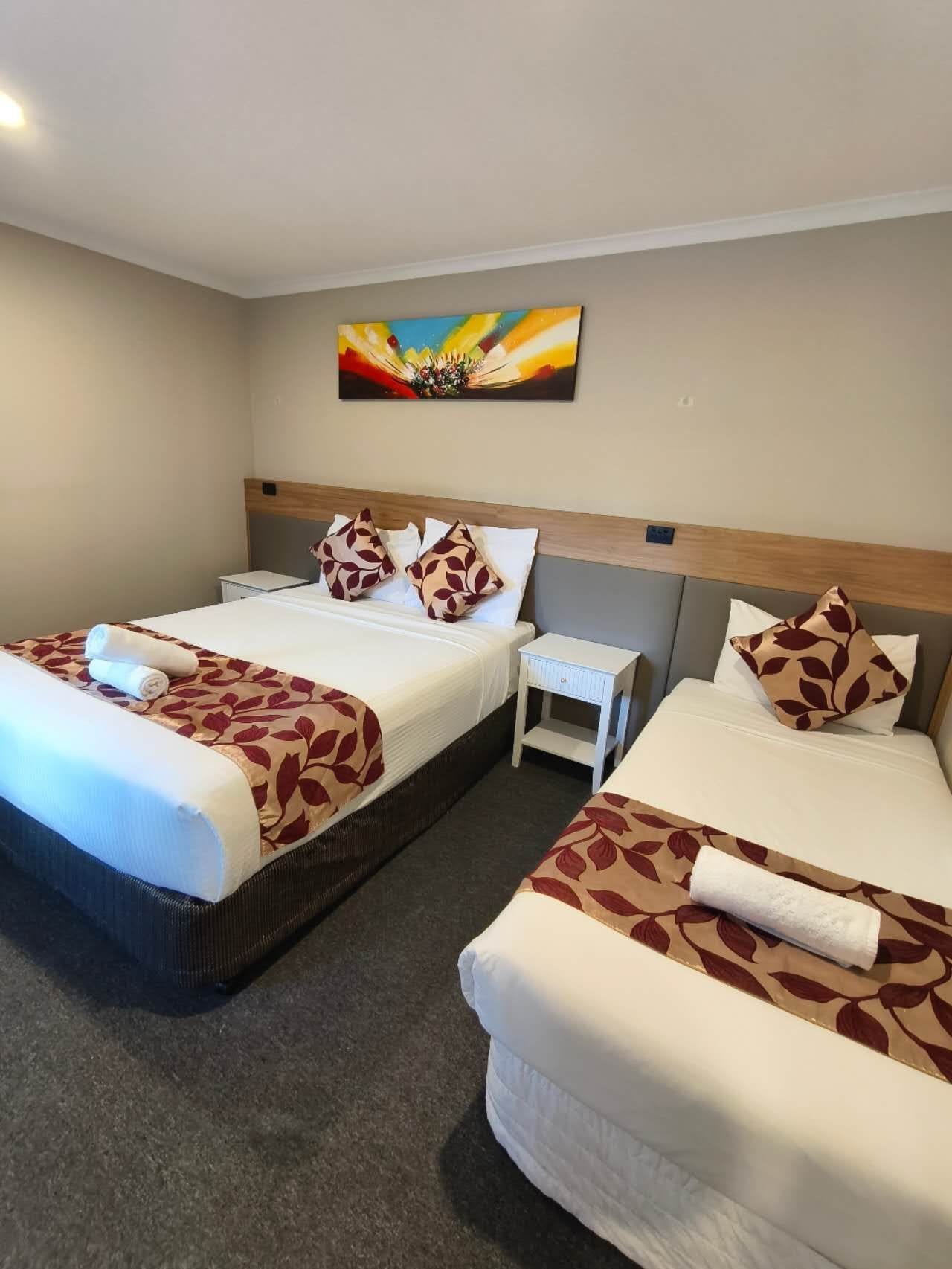 Habitación de hotel con dos camas, una mesita de noche, un cuadro en la pared y piso cubierto de alfombra.