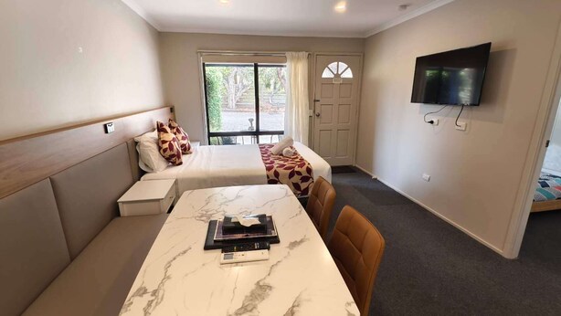 Una habitación de hotel compacta con cama, sofá, mesa de comedor y televisor montado en la pared.