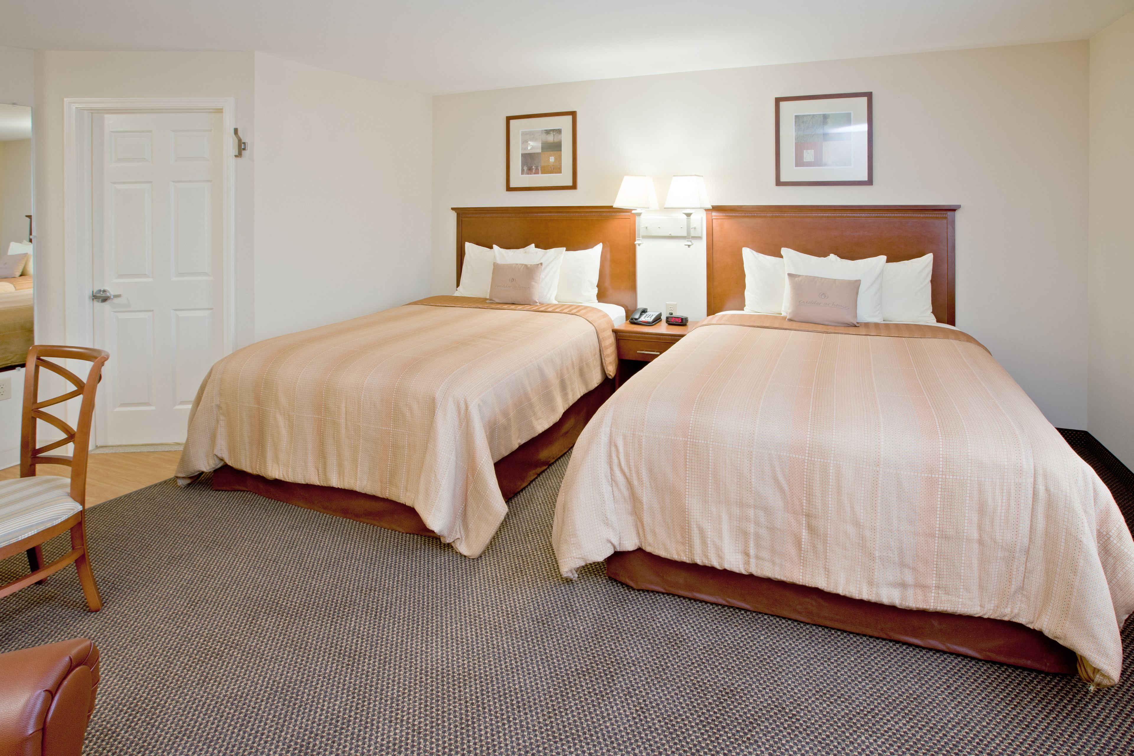 A hotel room with two beds, a wooden chair, a desk, and a door.