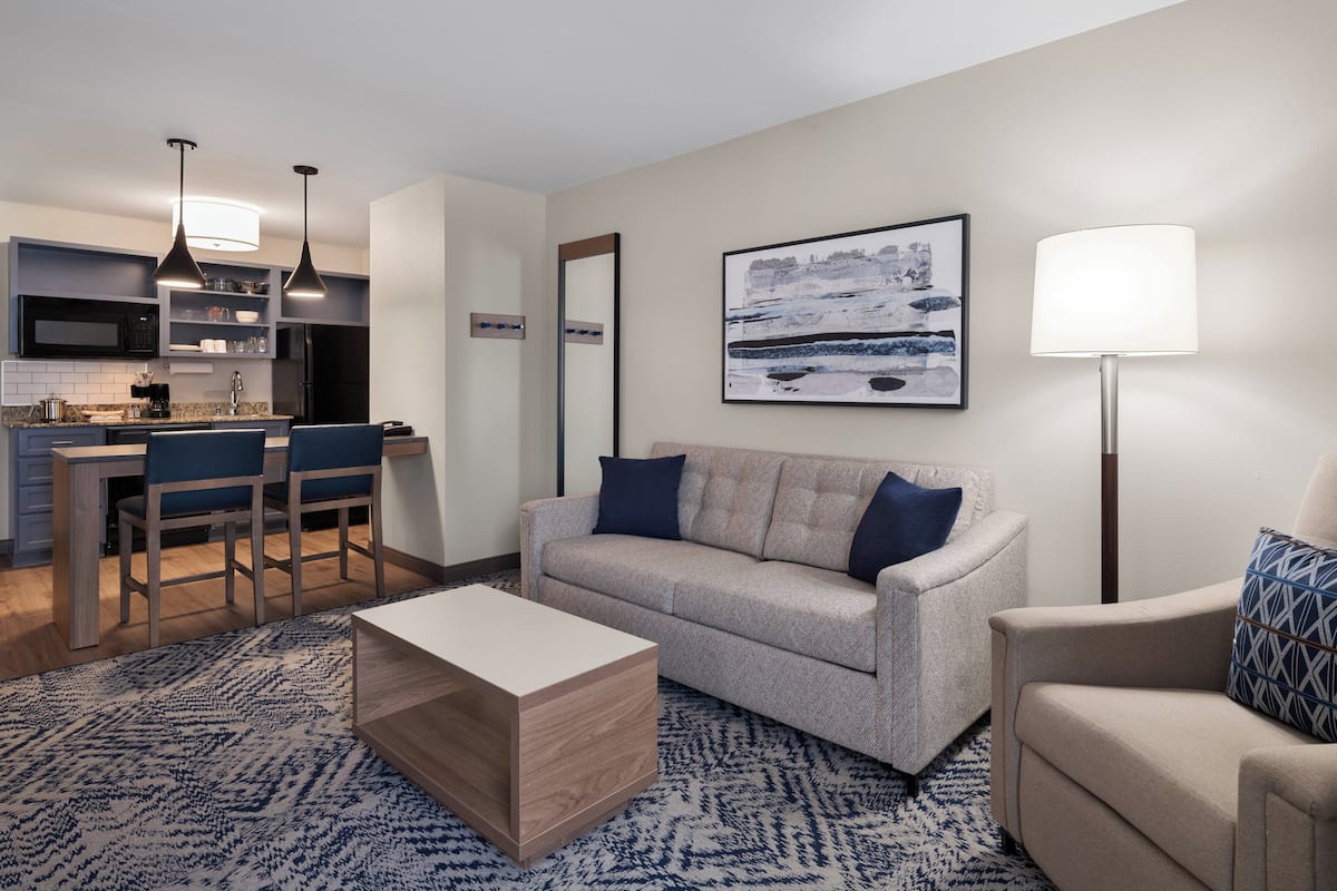 A modern living room with a sofa, coffee table, and a dining area with chairs and a kitchen in the background.