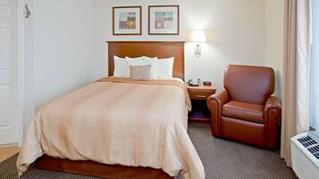 A hotel room with a large bed, a brown leather chair, a nightstand, a lamp, and a wall-mounted heater.