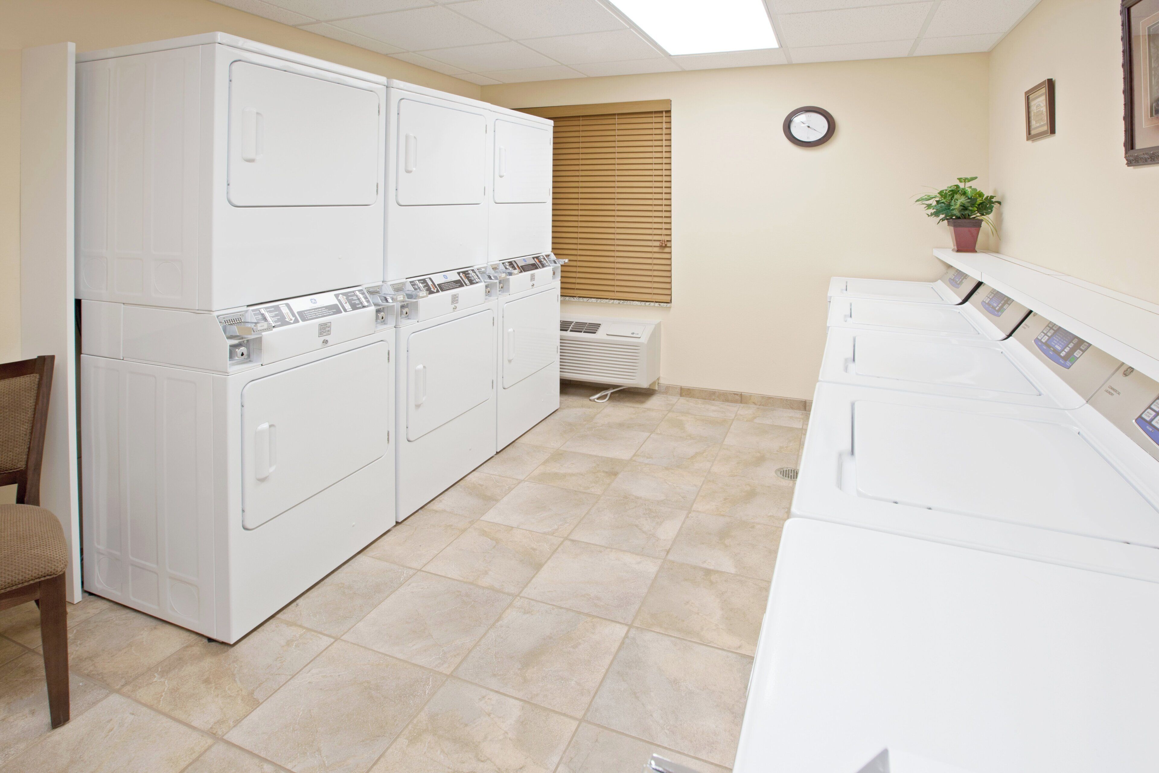 A laundry room with stacked washers and dryers, a clock on the wall, and a potted plant.