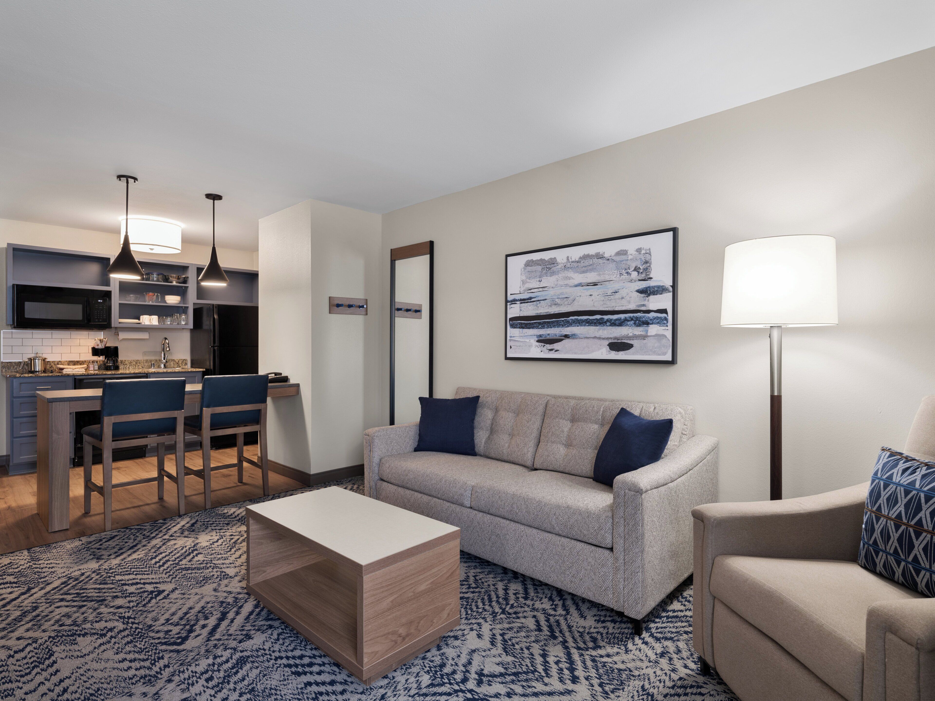 A modern living room with a sofa, coffee table, and a dining area with chairs and a kitchen in the background.