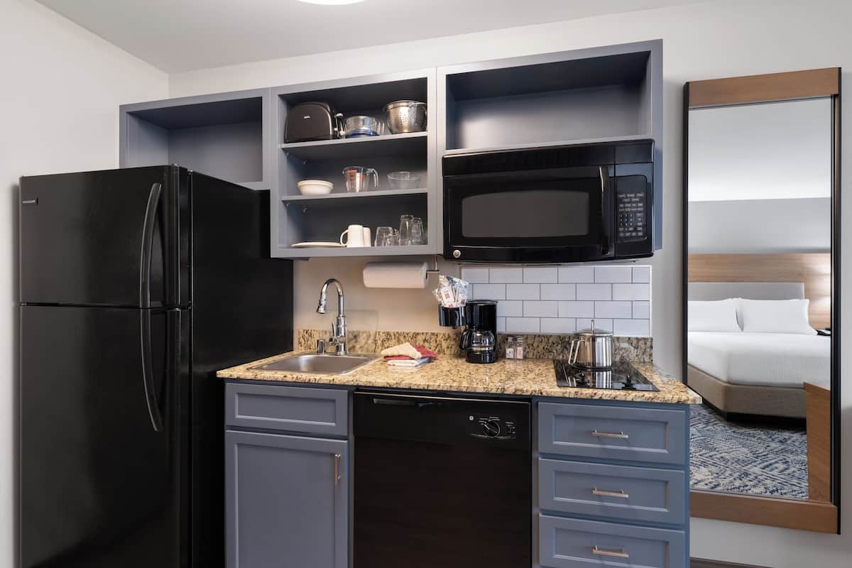 A compact hotel kitchen with a black refrigerator, a microwave, a coffee maker, and a sink.