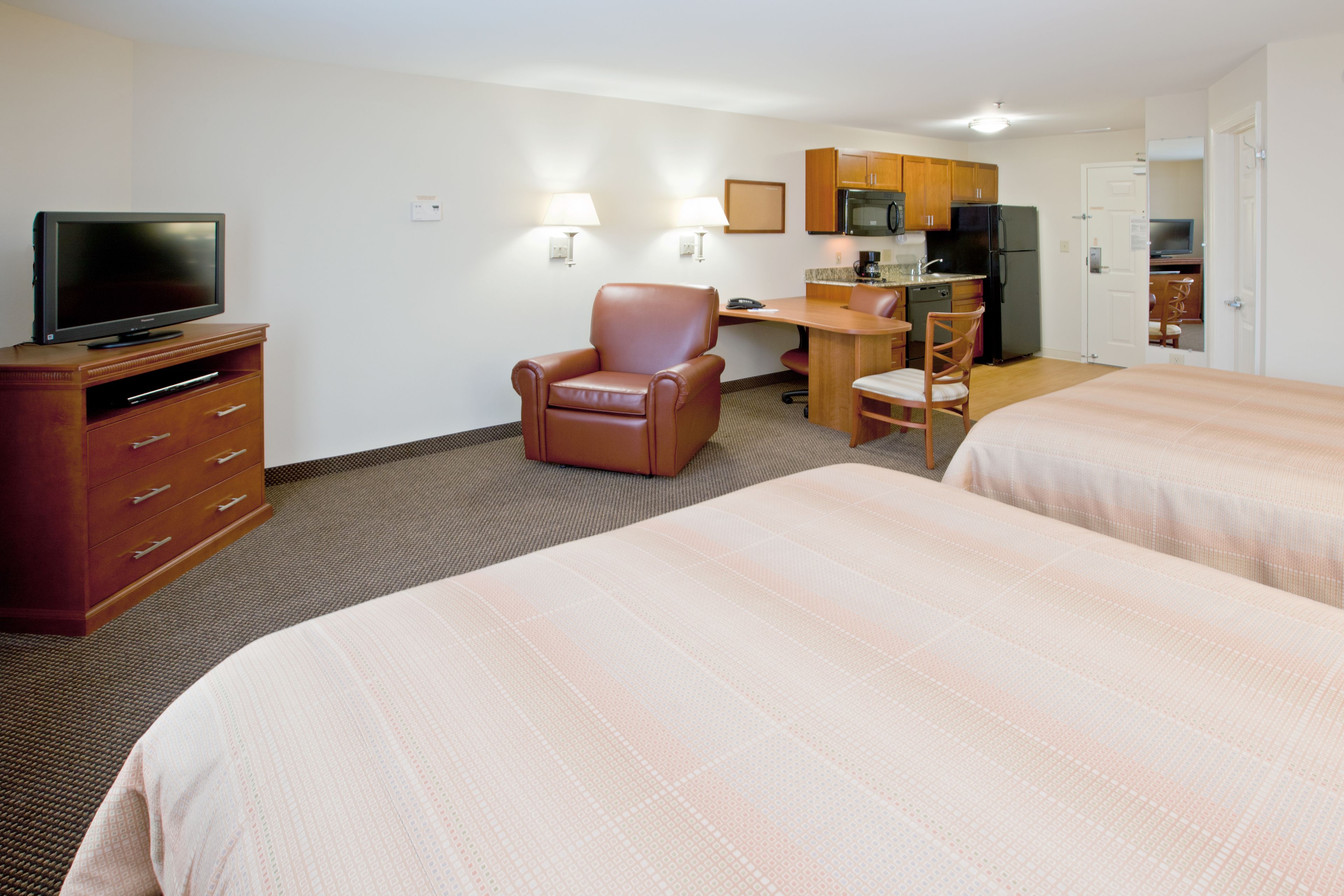 A hotel room with two beds, a desk, a chair, a television, and a kitchenette.