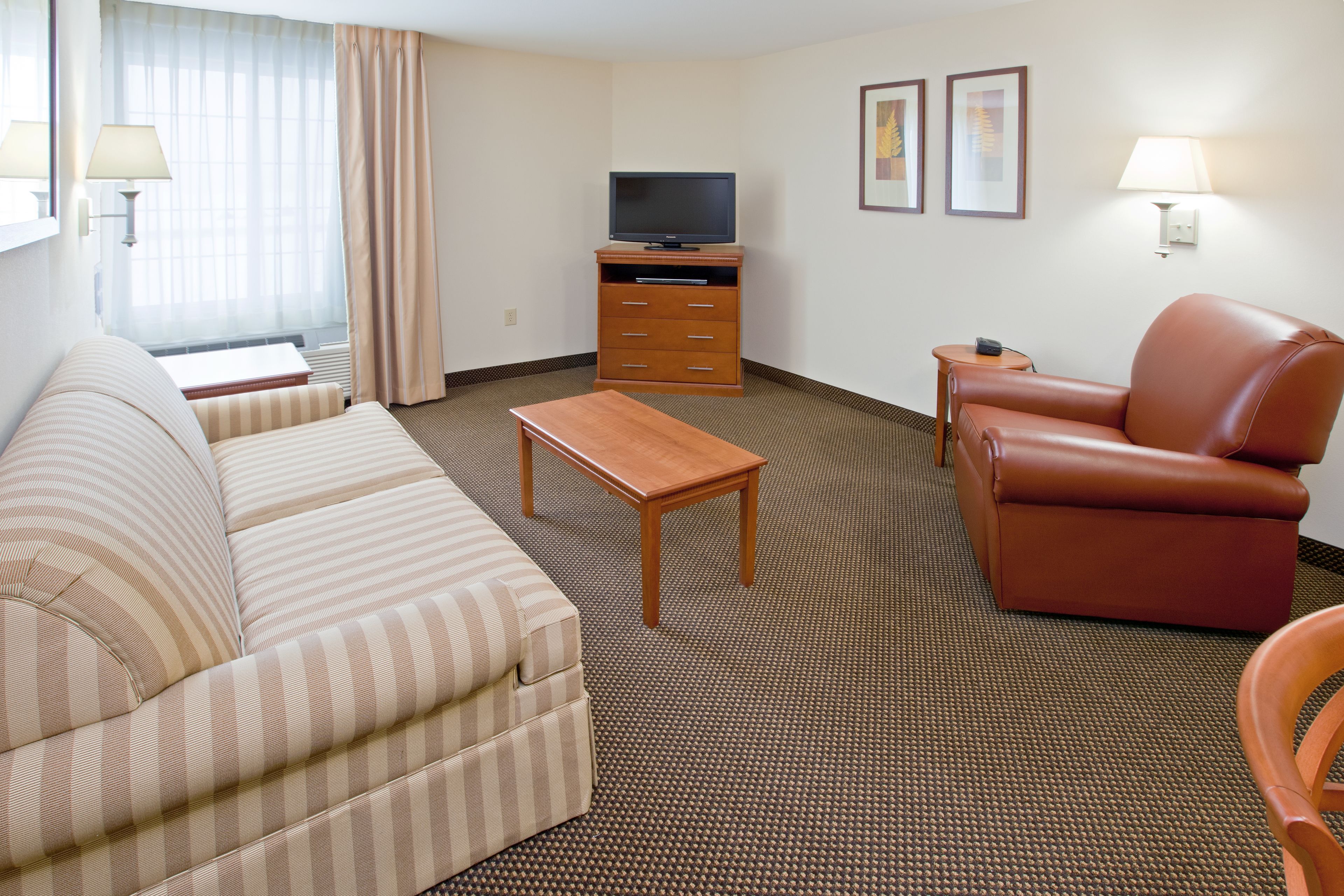 Een hotelkamer met een gestreept sofa, een leren fauteuil, een houten salontafel, een televisie op een houten voetstuk, en twee wandlampen.