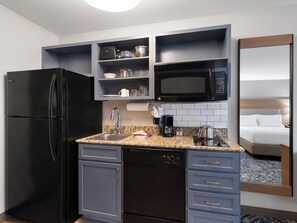 A compact hotel kitchen with a refrigerator, microwave, coffee maker, and a sink.