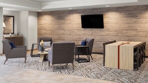 Een moderne hotelkamer met een houten accentmuur, een flatscreen televisie en een zithoek met een houten tafel en stoelen.
