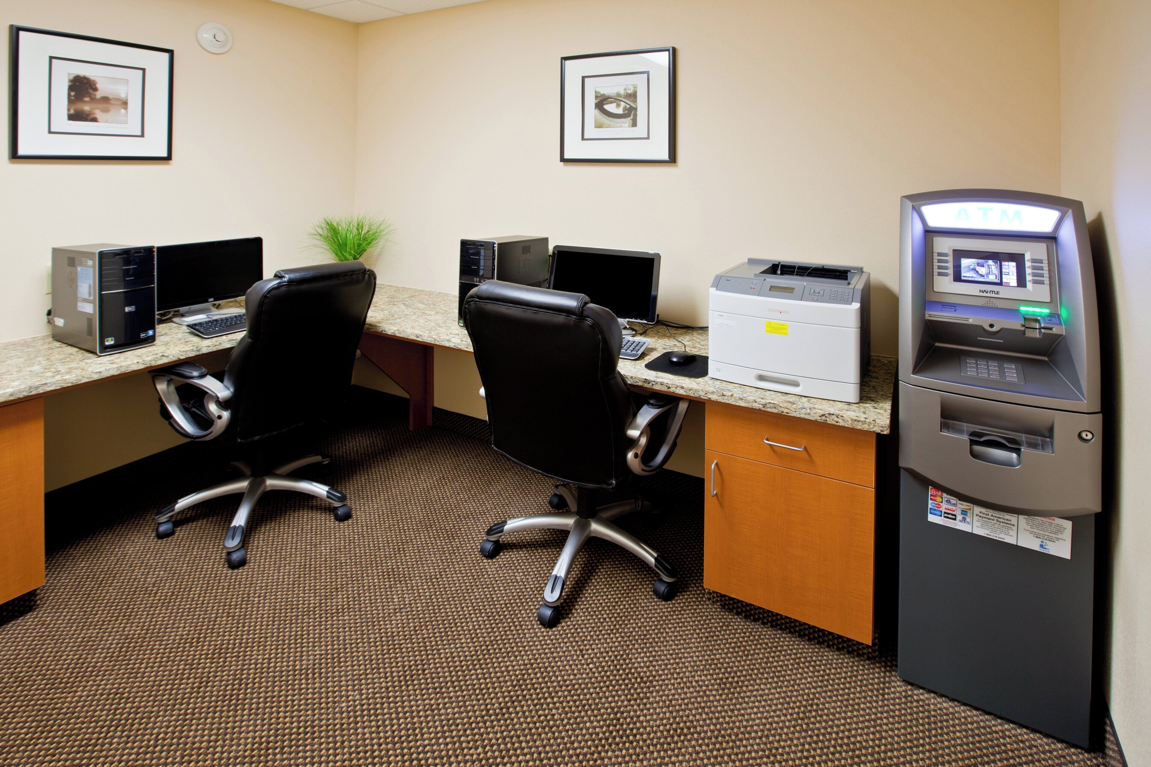 A hotel office with two desks, computers, chairs, a printer, and an ATM.