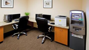 A hotel office with two desks, computers, chairs, a printer, and an ATM.