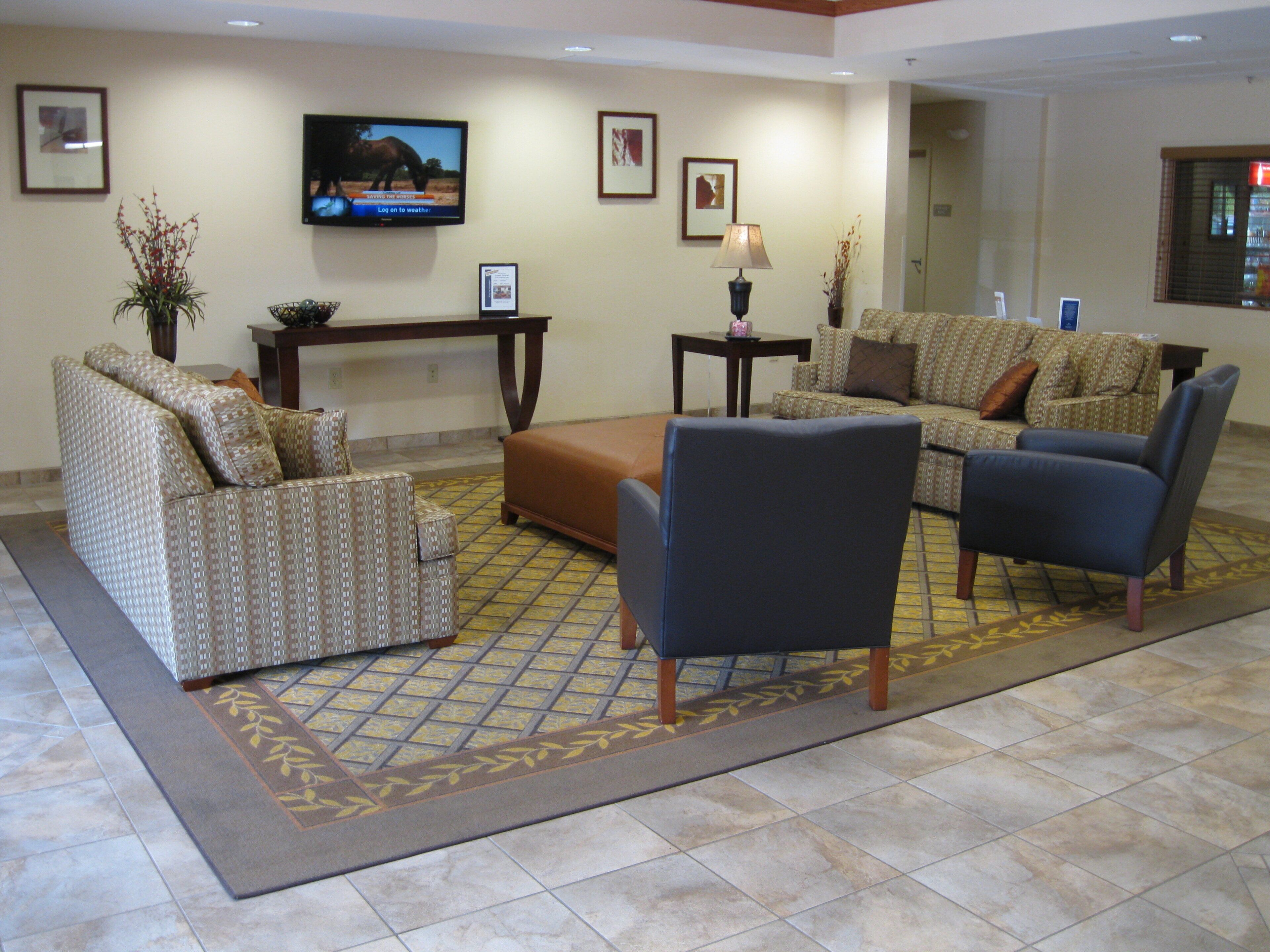 A hotel lobby with a reception desk, two sofas, a coffee table, and a television mounted on the wall.