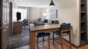 Ein modernes Hotelzimmer mit Essbereich, einer Couch, einem Fernseher und einem Bücherregal.