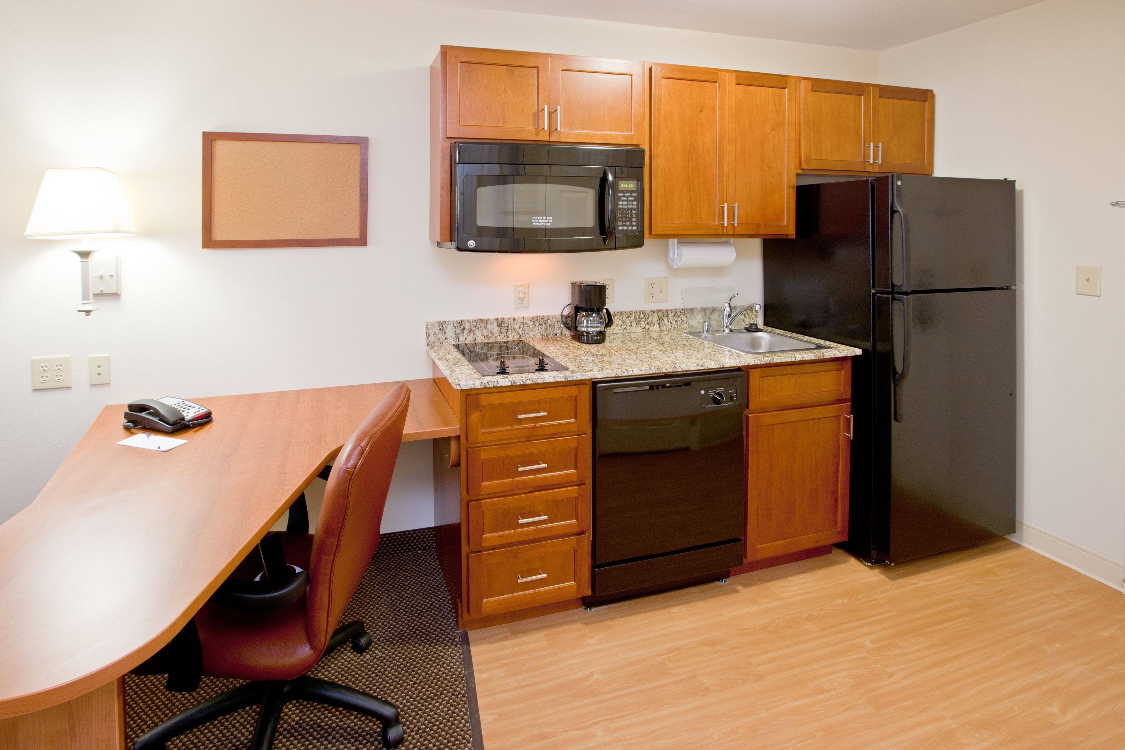 A compact kitchen with wooden cabinets, a microwave, a refrigerator, a coffee maker, and a sink.