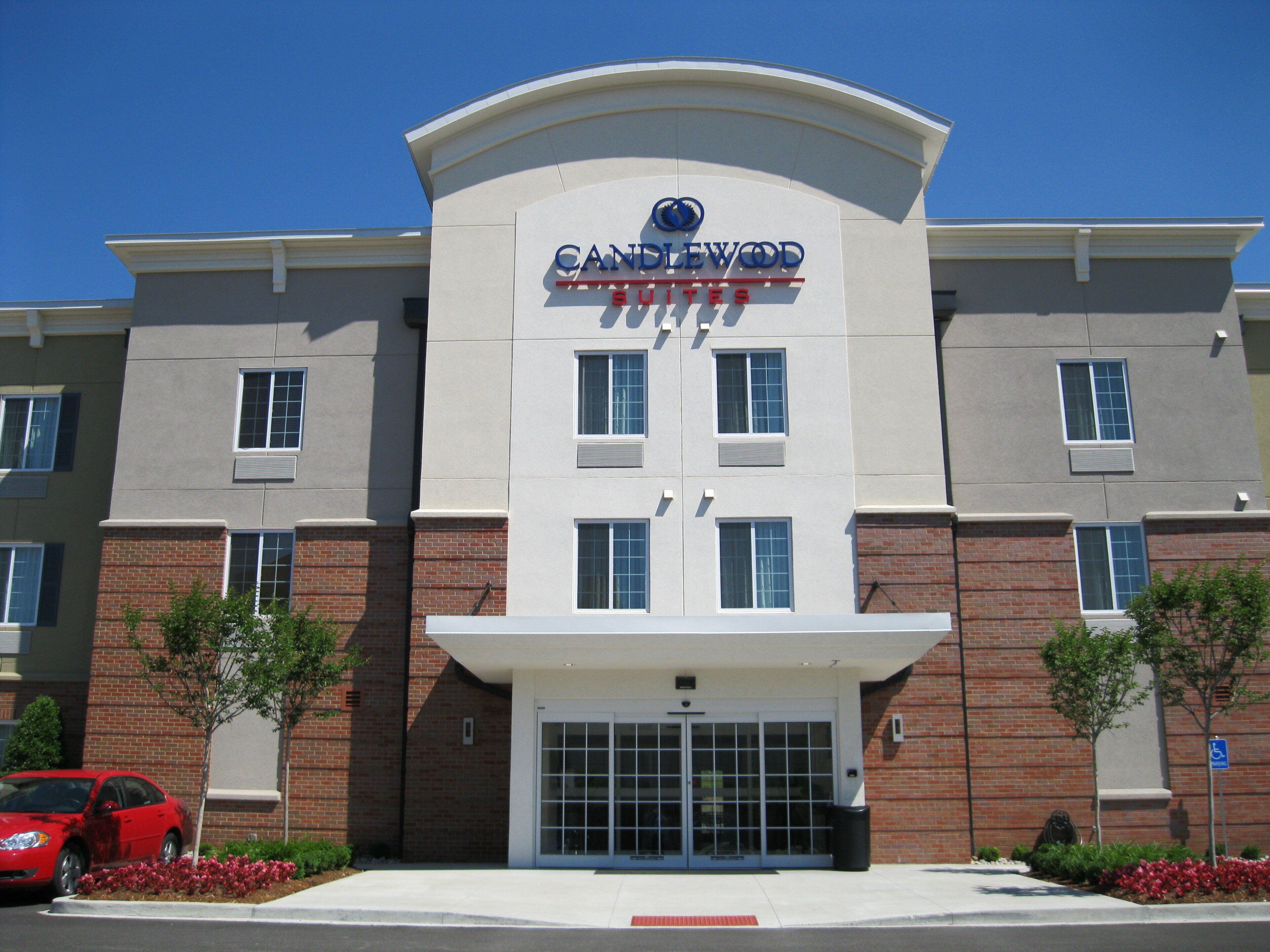 A hotel with a modern facade, a prominent entrance, and a parking area with a red car.