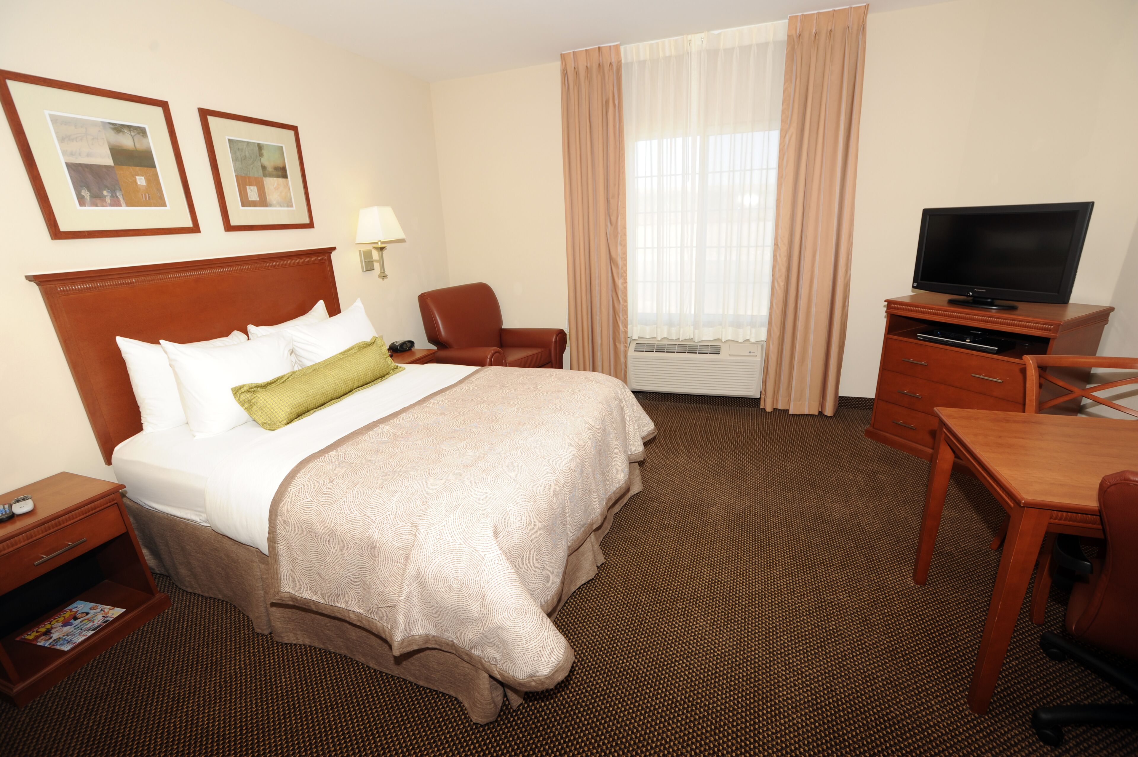 Una habitación de hotel con una cama grande, un escritorio con silla, televisión y ventana con cortinas.