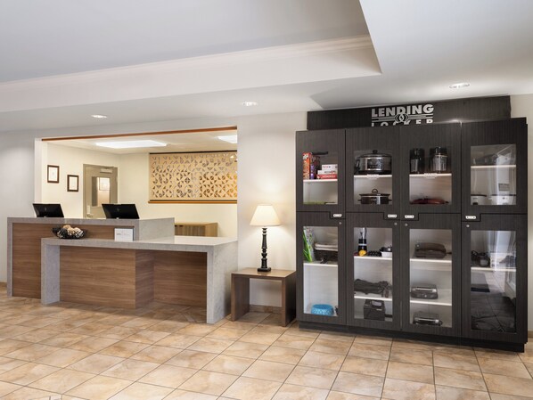 Uma área de recepção de hotel com um balcão moderno, uma placa com a palavra 'LENDING' e um armário com diversos objetos.