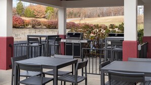 Een terras buiten met een barbecue, tafels en stoelen.