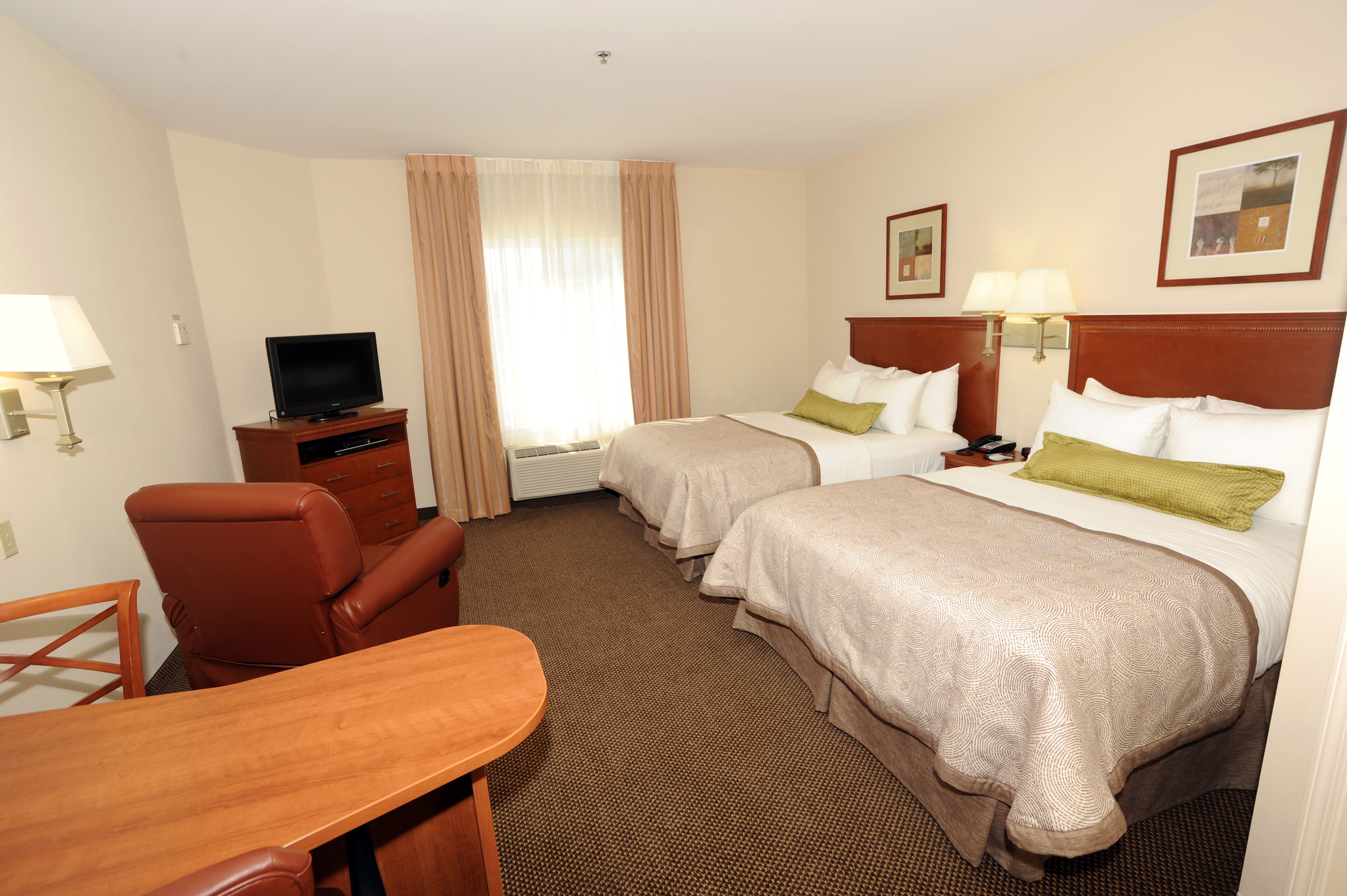 A hotel room with two beds, a desk, a chair, a television, and a window with curtains.