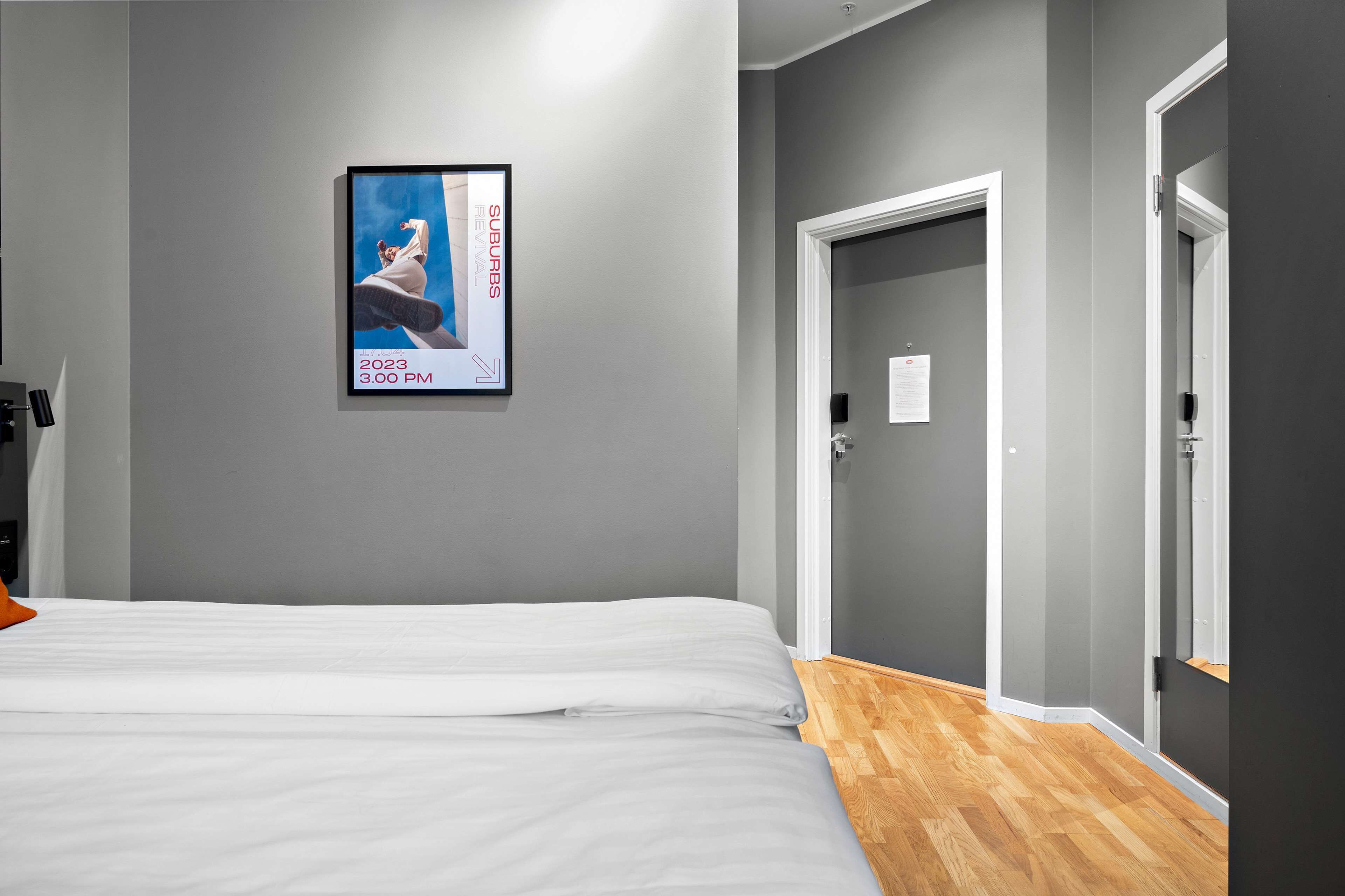 A hotel room with a bed, a poster on the wall, and a door to the right.