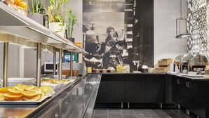 Zona de buffet con diversos alimentos, una estación de café y un gran mural en la pared.