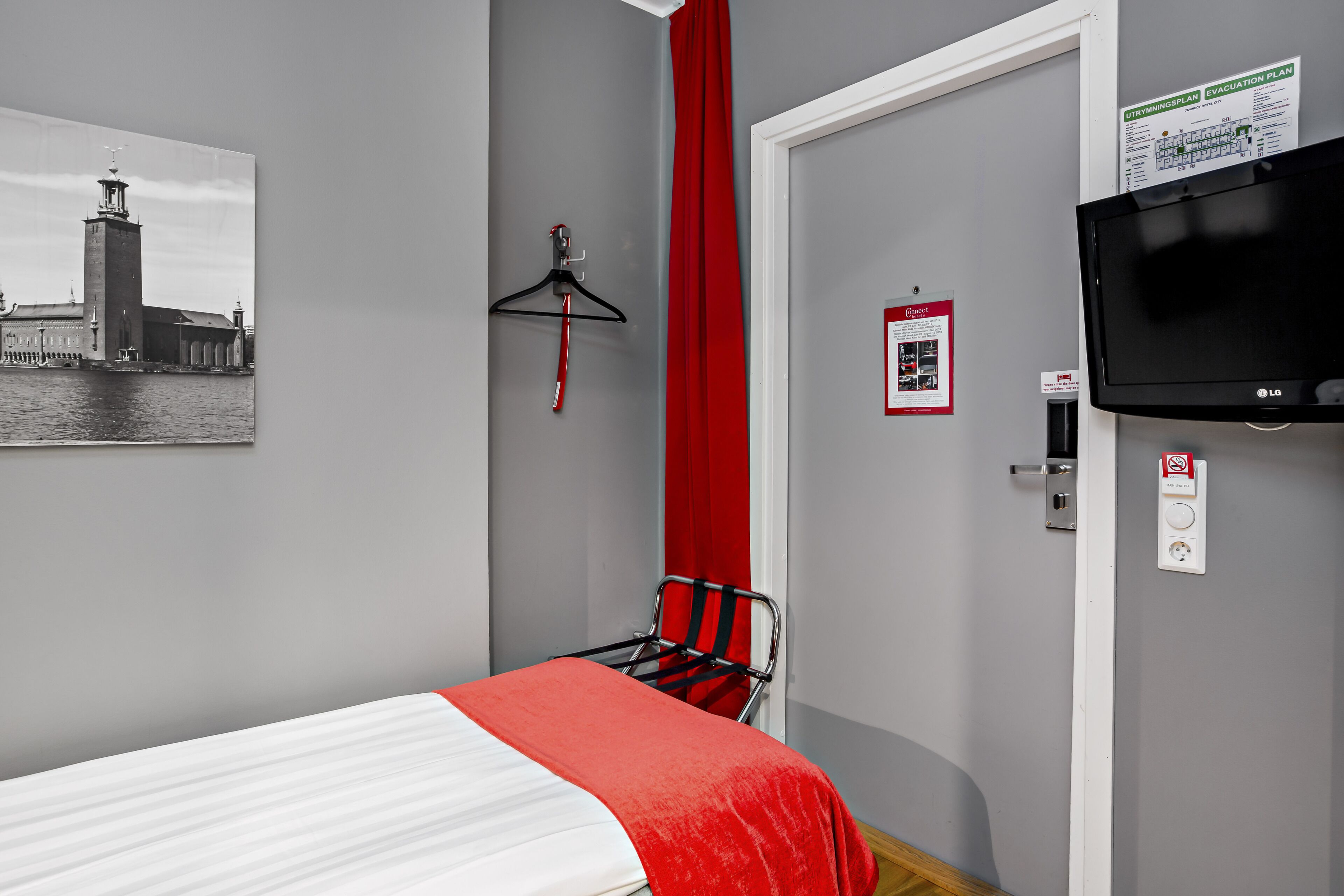 Habitación de hotel con cama, una silla, perchero, televisor y una imagen de un faro.