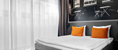 Quarto de hotel moderno com cama cinzenta, roupa de cama branca e almofadas laranja.