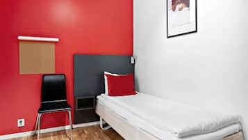 A small, single-bed room with a red wall, a black chair, and a white bed.