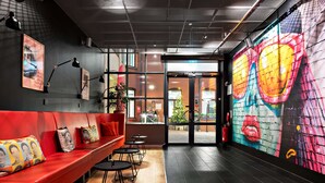 Un interior moderno con un sofá rojo, mesas negras y un mural colorido en la pared.